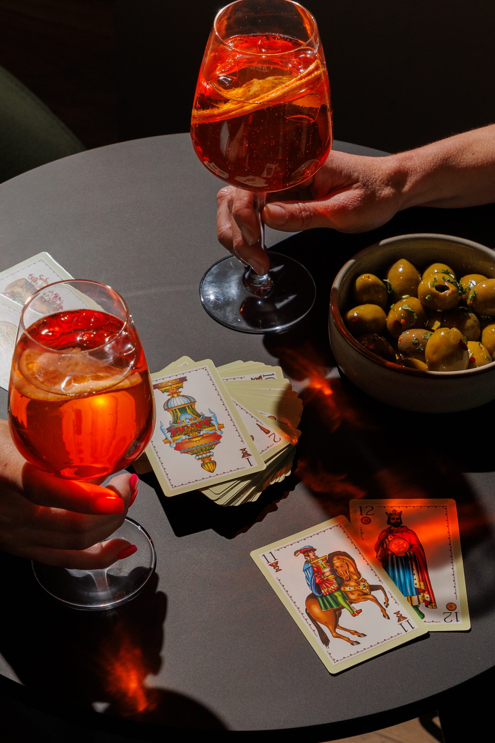 Aperol Spritz with olives and playing cards on a black table.